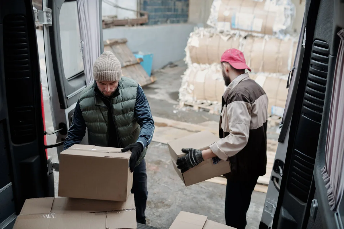 Two workers moving cardboard boxes beside a delivery van.
