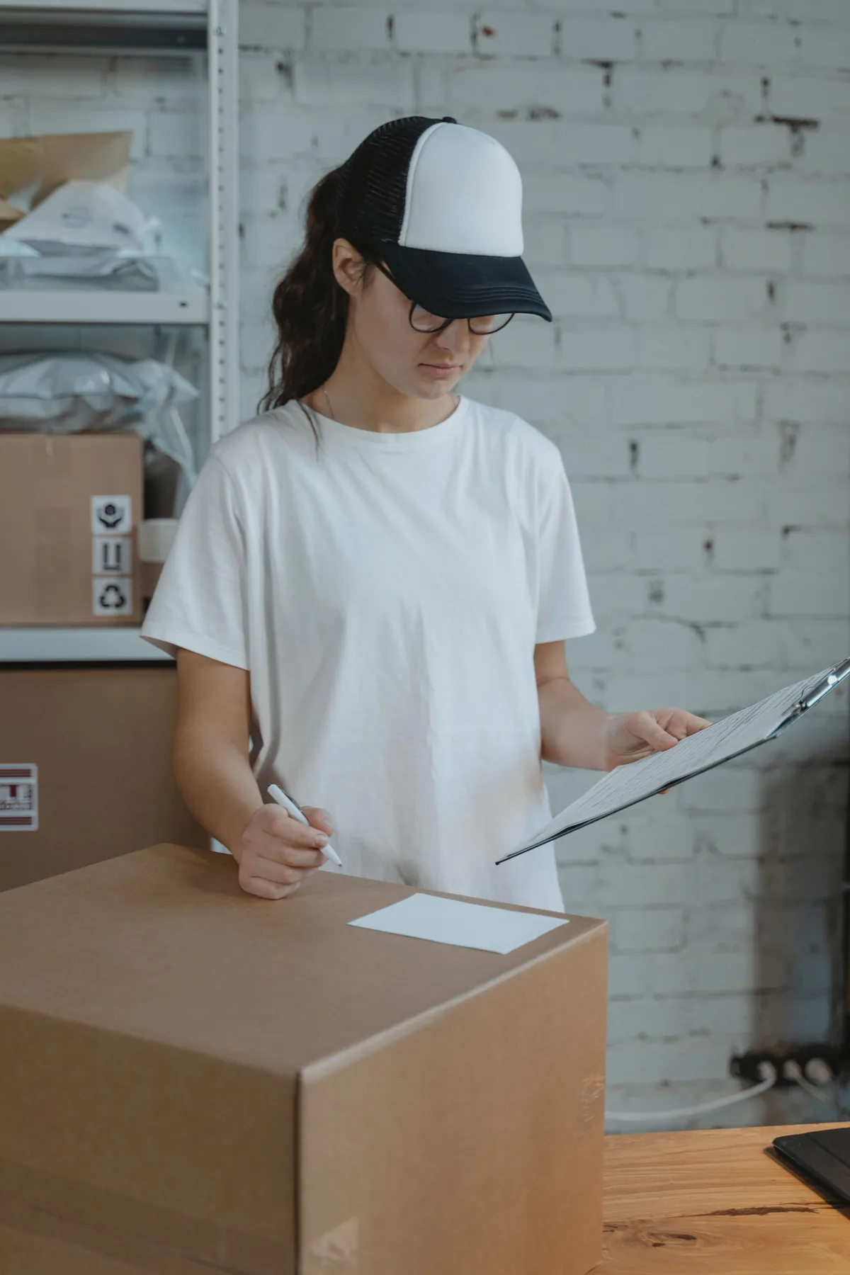Warehouse worker checking shipment details while writing on a cardboard box.
